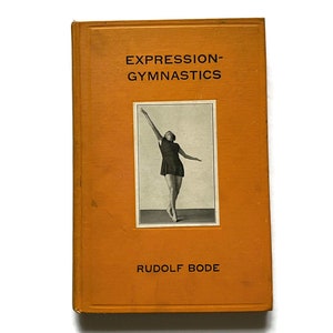 May include: An orange book titled "EXPRESSION-GYMNASTICS" by Rudolf Bode. The book cover features a black and white photo of a person in a dark dress with their arm raised. The book has a worn appearance.