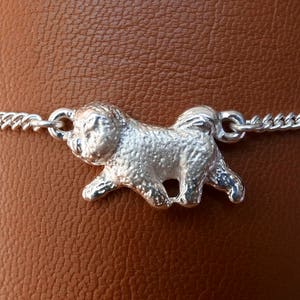 May include: A silver charm bracelet with a detailed silver dog charm. The dog charm is in a walking position with its head turned to the side.