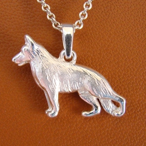 May include: Silver pendant necklace featuring a detailed German Shepherd dog charm. The dog is standing with its head turned to the side, and its tail is curled.