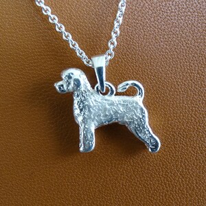 May include: Silver pendant necklace featuring a detailed, textured Portuguese Water Dog design. The dog is standing with its tail curled up.