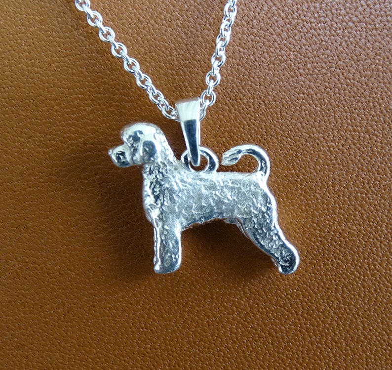May include: Silver pendant necklace featuring a detailed, textured Portuguese Water Dog design. The dog is standing with its tail curled up.
