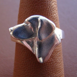 May include: A silver ring featuring a detailed, three-dimensional sculpture of a dog's head. The dog's head is facing left and has a smooth, polished finish.