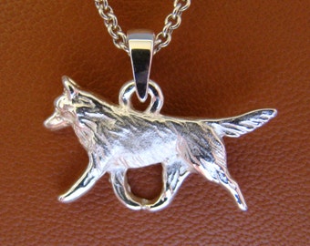 Puede incluir: Un collar con un colgante de plata que presenta una escultura tridimensional detallada de un perro corriendo. El colgante está unido a una cadena de plata.