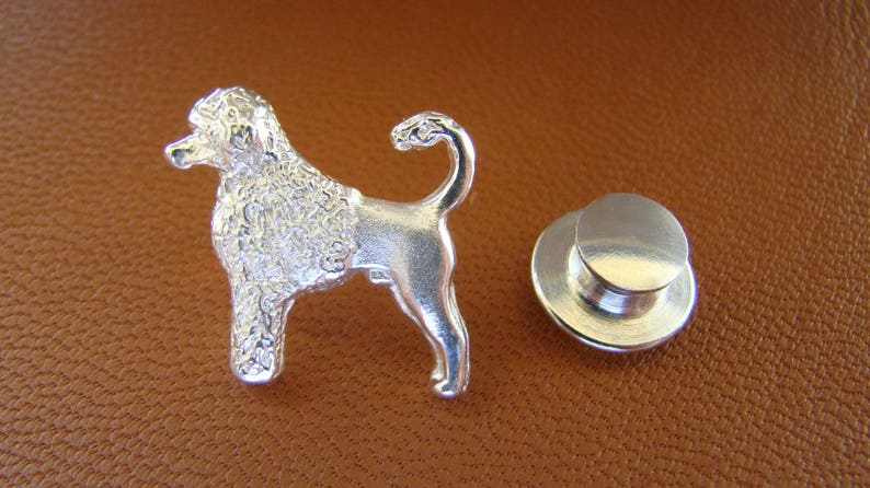 Puede incluir: Pin de perro caniche plateado con acabado texturizado. El pin tiene un cierre de poste y embrague.