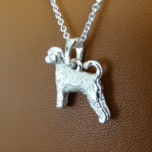 May include: Silver pendant necklace featuring a detailed, textured, silver dog charm. The dog is standing on all four legs with its tail curled up.
