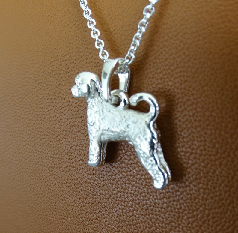 May include: Silver pendant necklace featuring a detailed, textured, silver dog charm. The dog is standing on all four legs with its tail curled up.