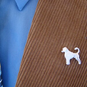 Puede incluir: Una chaqueta de pana marr&oacute;n con un broche de perro plateado. El broche es una silueta de un perro con la cola enroscada.