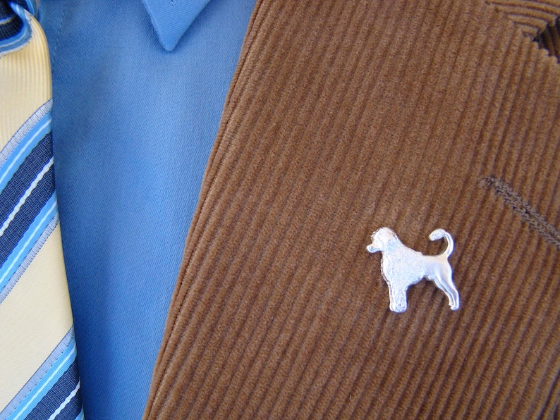 Puede incluir: Una chaqueta de pana marr&oacute;n con un broche de perro plateado. El broche es una silueta de un perro con la cola enroscada.