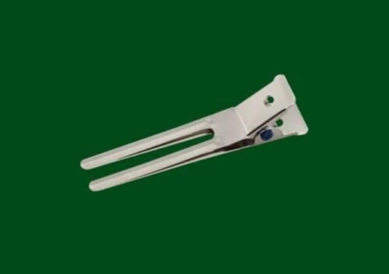 May include: A stainless steel can opener with a lever design. The can opener has two long, parallel arms and a hinged section with a small blue rivet. The background is a solid, dark green.