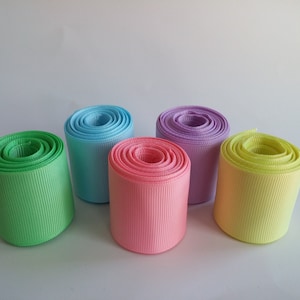 May include: Five spools of ribbon in different pastel colors: green, light blue, pink, lavender, and yellow. The ribbon is rolled up and ready to be used for crafting or decorating.