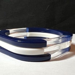 May include: A stack of three bangles. The top and bottom bangles are navy blue, and the middle bangle is white. The center of the bangles are clear. The bangles are stacked on top of each other.