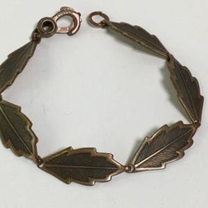 May include: A copper bracelet with a leaf design. The bracelet is made of a series of connected leaves, each with a detailed etched pattern.