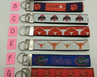 May include: Seven different keychains with various college logos. The keychains are made of orange, blue, red, and white ribbon with black trim. The logos include Clemson Tigers, Ohio State Buckeyes, Texas Longhorns, Florida Gators, and South Carolina Gamecocks.
