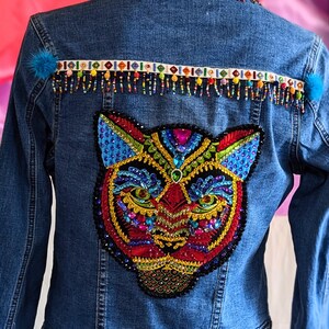 May include: A blue denim jacket with a colorful beaded trim and a large embroidered tiger face on the back.