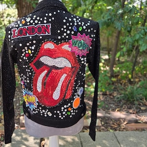May include: A black jacket adorned with numerous clear rhinestones, featuring a large red and white sequined lips graphic on the back. The design includes the text LONDON in red, a pink WOW speech bubble, and a yellow POW speech bubble.