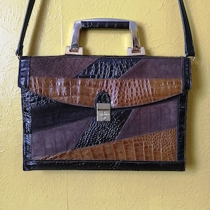 Peut inclure: Une mallette en cuir marron avec un design patchwork. La mallette a une poignée supérieure et une bandoulière. La bandoulière est en cuir noir.