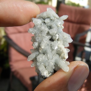 Puede incluir: Un grupo de cristales de cuarzo transparente con una formación espinosa e irregular. Los cristales se sostienen entre los dedos, mostrando su calidad translúcida y su apariencia natural y sin pulir. El cuarzo tiene un aspecto claro, casi esmerilado.