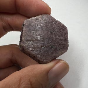 May include: A rough, hexagonal, dark purple ruby crystal with a natural, unpolished finish.