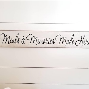 May include: White wooden sign with black cursive text that reads "Meals & Memories Made Here".