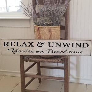 Peut inclure: Une pancarte en bois blanc avec du texte noir qui dit "Relax & Unwind You're on Beach time".