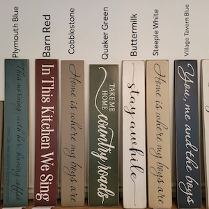 Peut inclure: Dix panneaux en bois avec diff&eacute;rentes citations et couleurs. Les panneaux sont peints dans des tons de bleu, vert, rouge, blanc et marron. Les panneaux pr&eacute;sentent des citations telles que "Home is where my boys are", "Stay awhile", "Take me home, country roads", et "In this kitchen we sing".