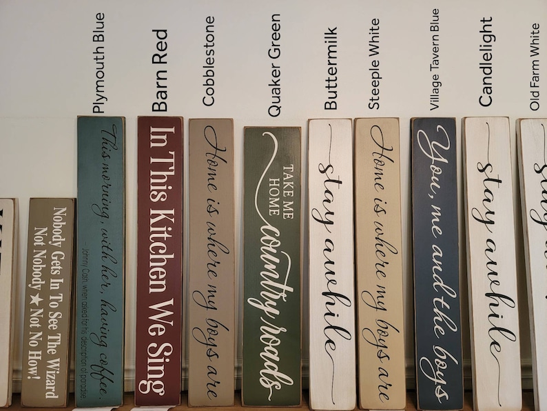 Peut inclure: Dix panneaux en bois avec diff&eacute;rentes citations et couleurs. Les panneaux sont peints dans des tons de bleu, vert, rouge, blanc et marron. Les panneaux pr&eacute;sentent des citations telles que "Home is where my boys are", "Stay awhile", "Take me home, country roads", et "In this kitchen we sing".