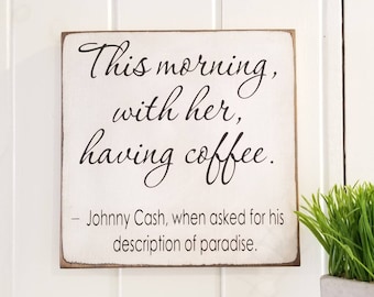 May include: White wooden sign with black text that reads "This morning, with her, having coffee."  The text is attributed to Johnny Cash, who said it was his description of paradise.