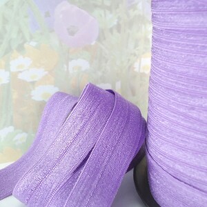 May include: A spool of lavender purple elastic with a shimmery finish. The elastic is folded in half and the spool is visible in the background.