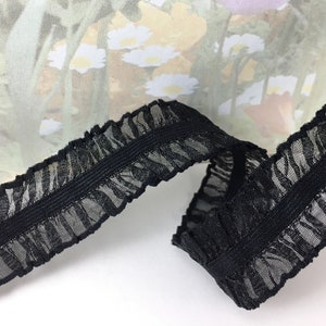 May include: Black elastic trim with a ruffled edge and a silver shimmer. The trim is approximately 1 inch wide.