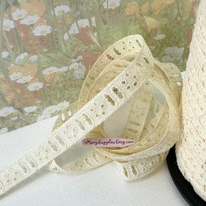 May include: A spool of off-white cotton lace trim with a delicate floral pattern. The lace is approximately 1/2 inch wide and has a scalloped edge.