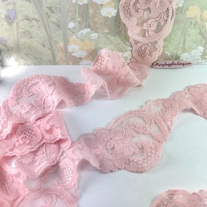 May include: Pink lace trim with a floral pattern. The lace is delicate and has a scalloped edge.