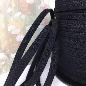 May include: Close-up of black elastic cord with a textured surface. The cord is wound into a spool.