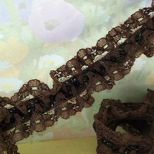 May include: Brown lace trim with a ruffled edge and a beaded center. The lace is delicate and has a vintage look.