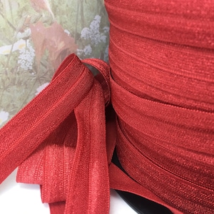 May include: A spool of red elastic with a shiny finish. The elastic is folded and stacked on the spool.