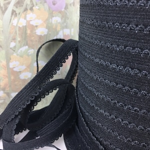 May include: Black elastic trim with a scalloped edge. The trim is folded and rolled up, showing the texture of the fabric.
