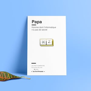 Op de afbeelding: Een gouden pin met een witte achtergrond met een toets van een computertoetsenbord met het symbool voor 'commando' en de letter 'Z'. De pin is op een witte kaart met de tekst 'Papa Homme dont l'informatique n'a pas de secret' en 'LES PIN'S NUMÉROTÉS You're the only one 42/500 los imprimousos.'