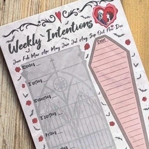 May include: A weekly intentions notepad with a gothic theme. The notepad features a black and white illustration of a gate with a coffin on the right side. The coffin is pink and has lines for writing. The notepad has a red heart with a couple inside and the text "Weekly Intentions" at the top. The months of the year are listed at the top of the notepad.