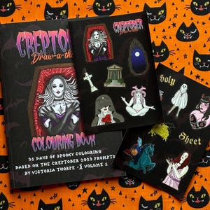 Pu&ograve; includere: Una collezione di articoli a tema Halloween, tra cui un libro da colorare e fogli di adesivi, disposti su un tessuto arancione con motivi di gatti neri e stelle. Il libro da colorare presenta una donna in una bara e gli adesivi illustrazioni spettrali.