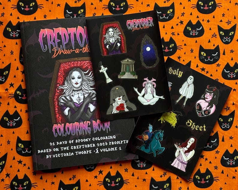 Pu&ograve; includere: Una collezione di articoli a tema Halloween, tra cui un libro da colorare e fogli di adesivi, disposti su un tessuto arancione con motivi di gatti neri e stelle. Il libro da colorare presenta una donna in una bara e gli adesivi illustrazioni spettrali.