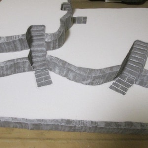 May include: A white foam board with three sets of gray stairs cut into the surface. The stairs are arranged in a curved pattern.