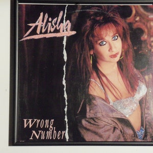Puede incluir: Una portada de álbum en blanco y negro con una mujer de pelo rojo largo que lleva un top de lentejuelas plateadas y una chaqueta de cuero negra. El título del álbum es "Alisha Wrong Number".