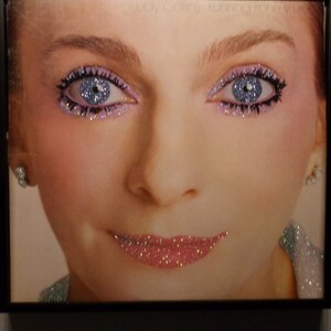 Peut inclure: Gros plan sur le visage d'une femme avec des yeux bleus et des lèvres roses. Ses paupières sont recouvertes de paillettes et ses lèvres sont recouvertes de paillettes.