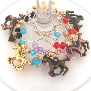 May include: Wine glass charms with horse and heart charms in gold, bronze, and turquoise. The charms are accented with colorful beads in red, purple, black, and gold. The charms are attached to silver wire rings.