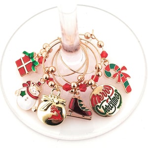 May include: Set of six gold-tone Christmas-themed wine glass charms. Each charm features a different design, including a snowman, a gift box, a candy cane, a reindeer, a pair of ice skates, and a circle with the text "Merry Christmas".