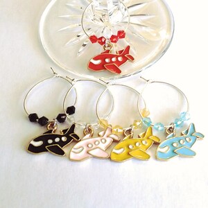 May include: Set of six wine glass charms featuring airplane designs in red, black, pink, yellow, and blue. Each charm has a gold-colored ring and a small bead accent.