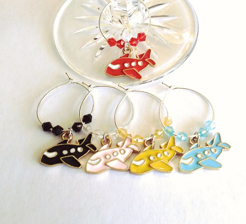 May include: Set of six wine glass charms featuring airplane designs in red, black, pink, yellow, and blue. Each charm has a gold-colored ring and a small bead accent.