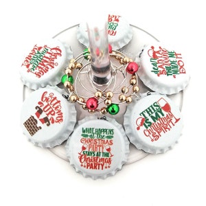 May include: Six white Christmas-themed bottle stoppers with red and green text and images. The stoppers feature phrases like "Bottoms Up", "This is my Christmas Spirit", and "What happens at the Christmas party stays at the Christmas party".