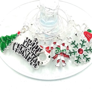 May include: Set of six silver Christmas-themed wine glass charms. The charms feature a green Christmas tree, a red and white candy cane, a red and green snowflake, a red bell, a silver ornament, and a charm with the words "Merry Christmas" in black.