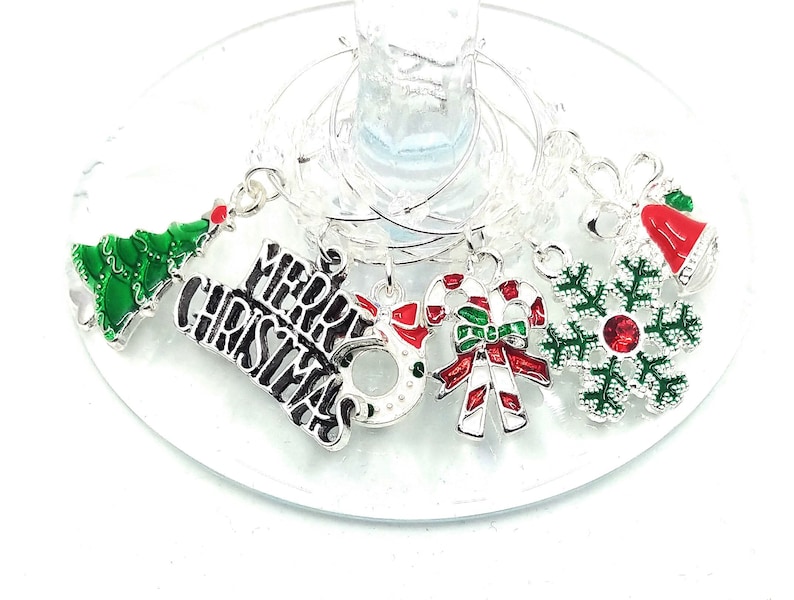 May include: Set of six silver Christmas-themed wine glass charms. The charms feature a green Christmas tree, a red and white candy cane, a red and green snowflake, a red bell, a silver ornament, and a charm with the words "Merry Christmas" in black.