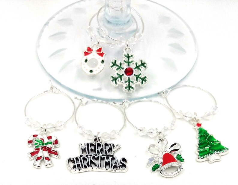 May include: Set of six silver Christmas themed wine glass charms. The charms feature a snowflake, a wreath, a candy cane, a Christmas tree, a bell with a red bow, and a charm that says "Merry Christmas".